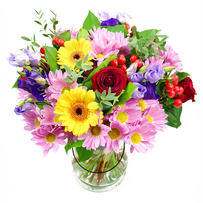 A lush, generously sized bouquet bursts from a clear glass vase, photographed against a clean white background so every flower and leaf is easy to imagine. Deep red roses sit at the centre like a beating heart, their velvety petals layered and full, exuding that timeless sense of romance and sincerity. Beside them, golden yellow gerbera daisies glow with cheerful faces and dark, textured centres, as if reflecting the lively energy of East Ham's markets on a busy day. Around this core, soft pink and lilac-hued daisies or chrysanthemums expand the bouquet outward, their many fine petals forming a cushion of pastel colour with bright yellow centres that gently punctuate the design. Threaded through are graceful stems of purple and lavender lisianthus, some fully open, others still in bud, their bell-shaped blooms and smooth, slightly curled petals adding a cool, sophisticated note. Between leaves and petals, clusters of round, glossy red hypericum berries peek out, providing playful dots of colour and a pleasant, tactile contrast to the soft flowers. The arrangement is wrapped in abundant greenery, from broad, dark green leaves to delicate, lighter sprigs that create a sense of movement, almost like a breeze moving through the trees near Central Park. The clear glass vase reveals the crisscross of neatly trimmed stems and fresh water, giving a glimpse of the careful, professional hand behind the design. The overall impression is one of joyful celebration and heartfelt thoughtfulness, a bouquet that would feel perfectly at home gracing a dining table off High Street North, welcoming guests to a home near Plashet Grove, or marking any special East Ham occasion with warmth and natural beauty.