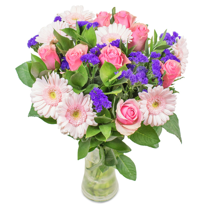 Vibrant and meticulously arranged, this floral bouquet from East Ham Flowers captures the essence of both modern elegance and natural abundance. Displayed in a transparent glass vase against a clean, luminous background, the bouquet features around eight velvety pink roses; their petals gently unfurl in classic, spiral formations, radiating with youthful charm. Complementing the roses are six pale pink Gerbera daisies-each with wide, rounded heads and lighter, subtly blushed centres, reminiscent of blooms seen in local East Ham gardens during spring. Punctuating the arrangement are lively clusters of vivid purple statice, their textures slightly feathery, lending depth and contrast to the softer petals. Wrapped in deep green foliage, the bouquet's foundation flows with exuberant freshness, the leaves appearing dewy and vibrant as if just gathered from an East Ham morning market near Ron Leighton Way. The clear vase reveals crisscrossed stems submerged in pristine water, speaking to the arrangement's freshness-ready for delivery or display. This composition, ideal for birthdays, anniversaries, or as an uplifting home accent, radiates warmth and affectionate thoughtfulness, bringing a piece of East Ham's flourishing spirit indoors.